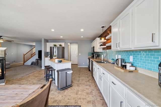 kitchen featuring stainless steel appliances, baseboards, white cabinetry, a kitchen island, and a glass covered fireplace