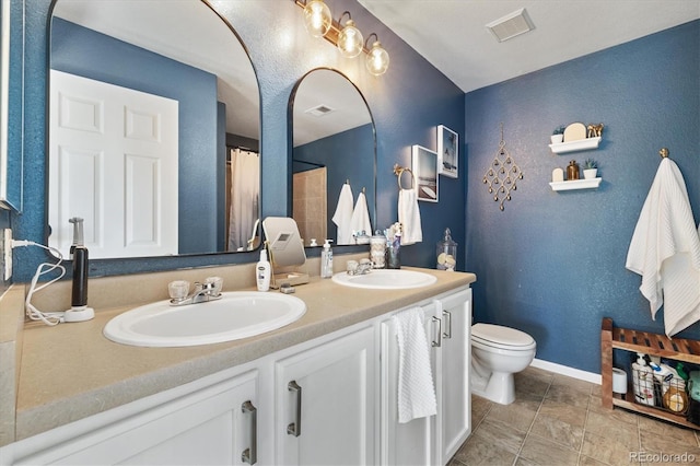 full bath featuring toilet, double vanity, a textured wall, and baseboards