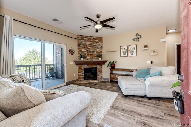 living room with ceiling fan, light hardwood / wood-style flooring, and a stone fireplace