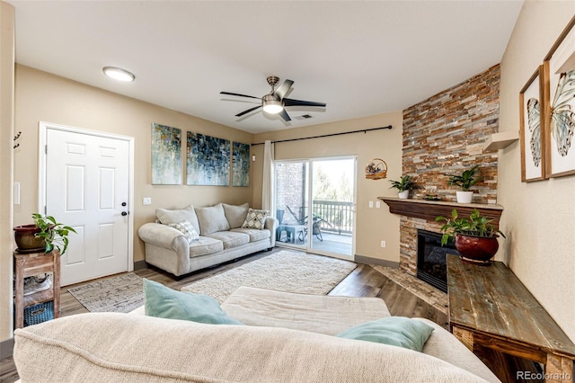 living room with ceiling fan, hardwood / wood-style flooring, and a stone fireplace