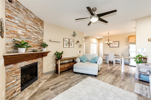 living room featuring a fireplace, light wood-type flooring, and ceiling fan with notable chandelier