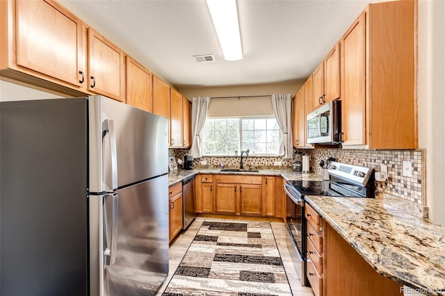 kitchen featuring appliances with stainless steel finishes, sink, backsplash, light stone counters, and a textured ceiling