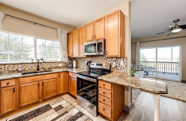 kitchen featuring light stone countertops, appliances with stainless steel finishes, tasteful backsplash, sink, and light hardwood / wood-style flooring