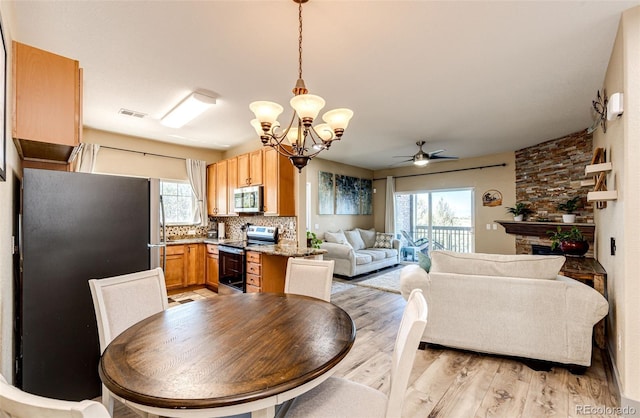 dining space featuring a fireplace, ceiling fan with notable chandelier, and light hardwood / wood-style flooring