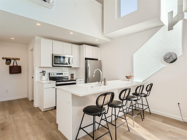 kitchen featuring a kitchen breakfast bar, stainless steel appliances, white cabinets, sink, and kitchen peninsula