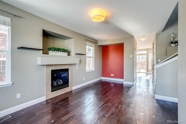 unfurnished living room featuring dark wood-type flooring and a tiled fireplace