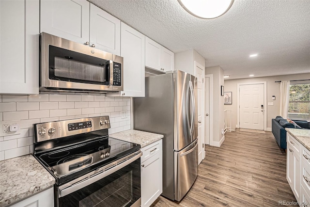 7005 Zenobia Pl, Westminster, CO 80030 - kitchen with decorative backsplash, a textured ceiling, white cabinets, light wood finished floors, and appliances with stainless steel finishes