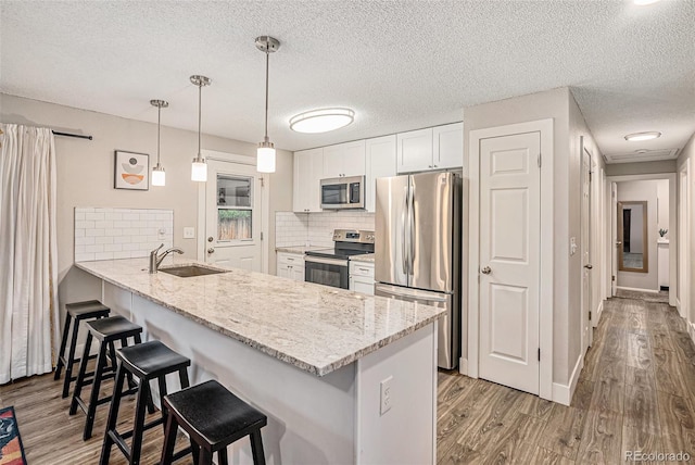 7005 Zenobia Pl, Westminster, CO 80030 - kitchen featuring a peninsula, wood finished floors, a breakfast bar, a sink, and stainless steel appliances