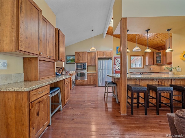 7585 Native Dancer Trl, Evergreen, CO 80439 - kitchen with appliances with stainless steel finishes, brown cabinetry, dark wood-style flooring, a breakfast bar area, and tasteful backsplash