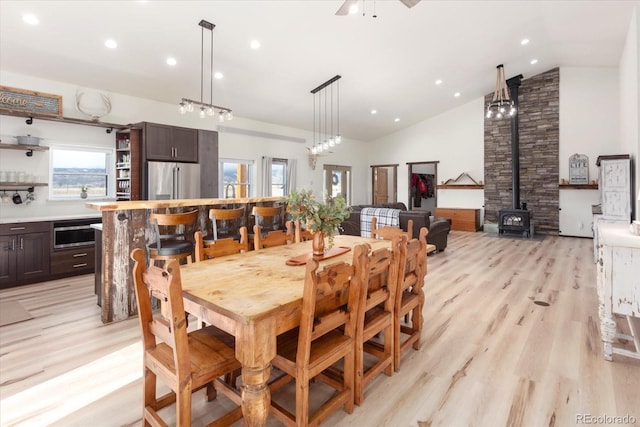 dining room featuring ceiling fan, high vaulted ceiling, a wood stove, and light wood-type flooring