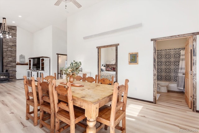 dining area featuring light wood-type flooring, high vaulted ceiling, ceiling fan, and a wood stove