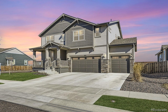 craftsman house with driveway, stone siding, an attached garage, and fence