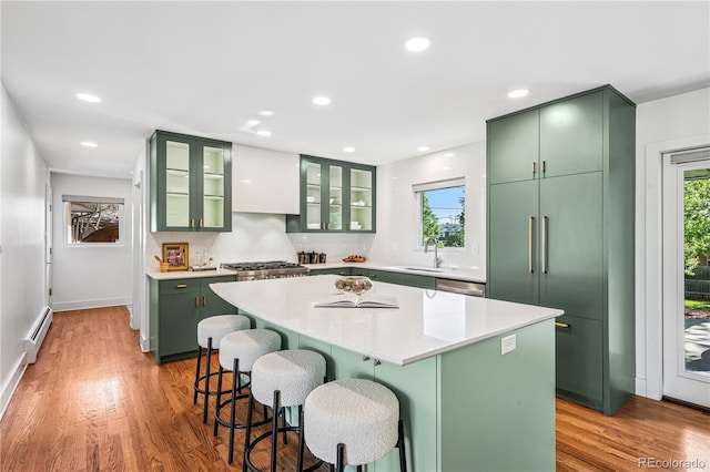 kitchen with green cabinets, a sink, a breakfast bar, light wood-style flooring, and a center island
