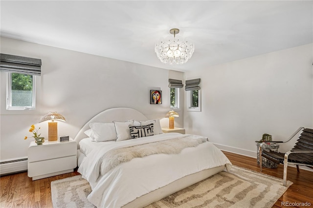bedroom featuring a chandelier, wood finished floors, baseboard heating, and baseboards