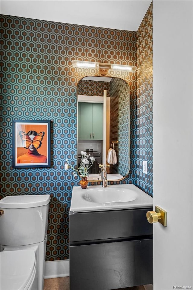 bathroom featuring wallpapered walls, vanity, toilet, and baseboards