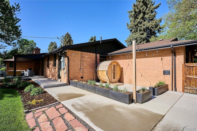 view of side of home with a patio area, brick siding, a chimney, and fence