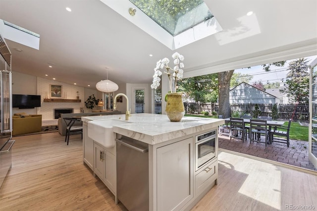 435 Ivanhoe St, Denver, CO 80220 - kitchen featuring dishwasher, a skylight, a brick fireplace, a center island with sink, and light wood finished floors