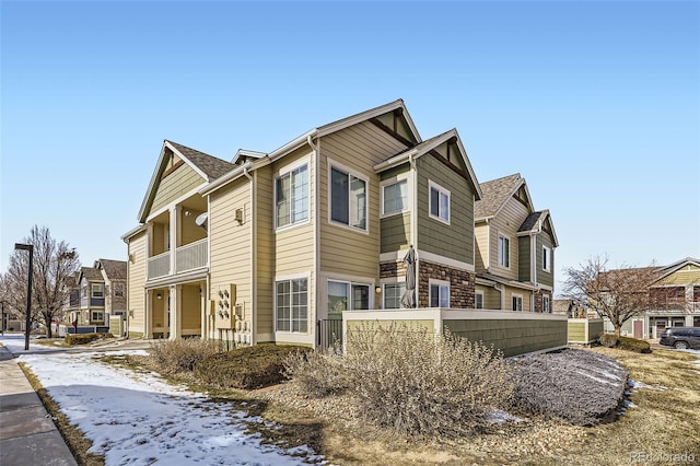 view of snowy exterior featuring a balcony, stone siding, and a shingled roof