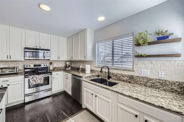 kitchen with stainless steel appliances, a sink, white cabinetry, and light stone countertops