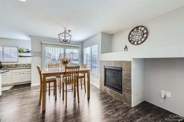 dining space featuring baseboards, a tile fireplace, dark wood-type flooring, a textured ceiling, and a chandelier