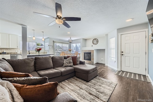 living room with dark wood finished floors, a tiled fireplace, a ceiling fan, a textured ceiling, and baseboards