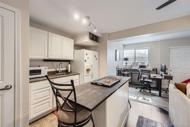 kitchen with white appliances, dark countertops, a sink, and white cabinetry