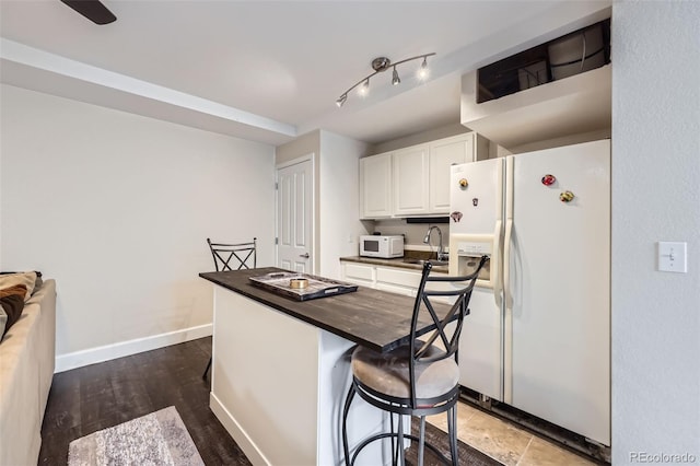 kitchen featuring white cabinets, a sink, butcher block countertops, white appliances, and baseboards