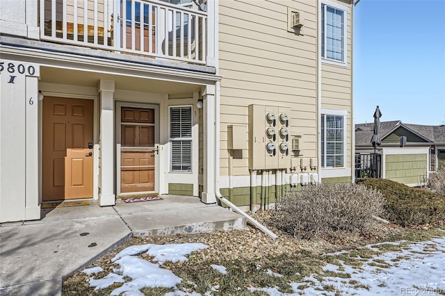 snow covered property entrance with a balcony