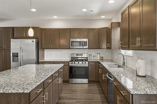 7956 Osage St, Denver, CO 80221 - kitchen with appliances with stainless steel finishes, dark wood-style flooring, light stone countertops, a kitchen island, and decorative backsplash