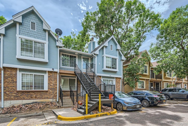 view of property with brick siding, stairway, and uncovered parking