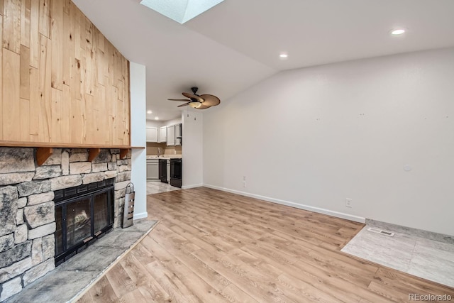 unfurnished living room featuring lofted ceiling with skylight, a fireplace, recessed lighting, and light wood-style flooring