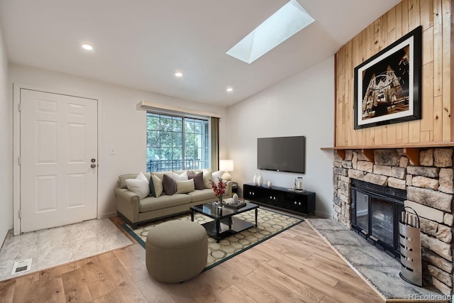 living room with vaulted ceiling with skylight, wood finished floors, visible vents, recessed lighting, and a fireplace