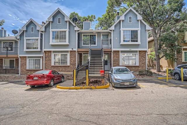 view of front of property featuring uncovered parking, a chimney, brick siding, and stairway