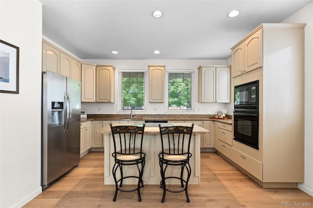 1901 S Union Pl, Lakewood, CO 80228 - kitchen with black appliances, a breakfast bar, recessed lighting, a kitchen island, and light wood-style floors