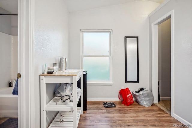 bathroom with hardwood / wood-style flooring, vaulted ceiling, and a tub