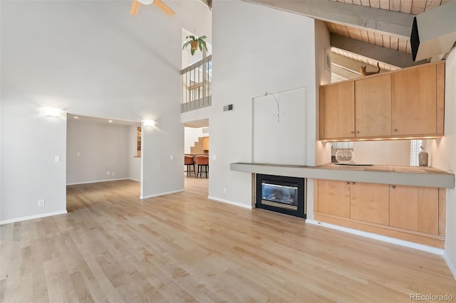 unfurnished living room featuring a glass covered fireplace, baseboards, light wood-type flooring, and ceiling fan