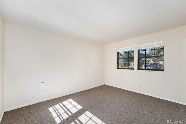 spare room with baseboards and dark carpet