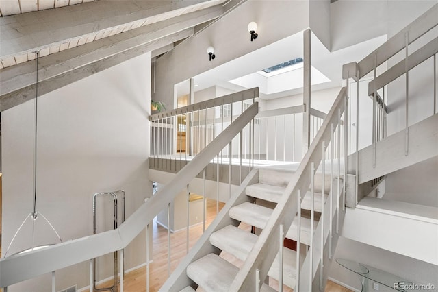 stairway featuring wood finished floors, a high ceiling, and a skylight