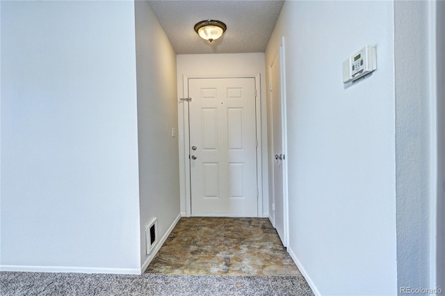 doorway to outside featuring a textured ceiling, baseboards, and stone finish floor