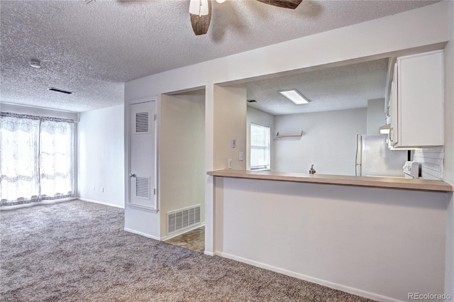 kitchen with ceiling fan, a textured ceiling, visible vents, freestanding refrigerator, and carpet flooring