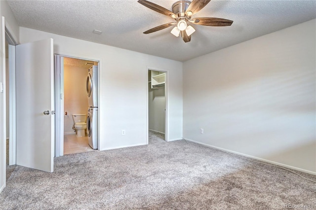unfurnished bedroom with a textured ceiling, carpet, baseboards, a spacious closet, and stacked washer and clothes dryer