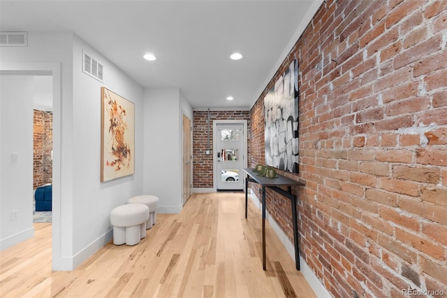 corridor featuring visible vents, light wood-style flooring, brick wall, and baseboards