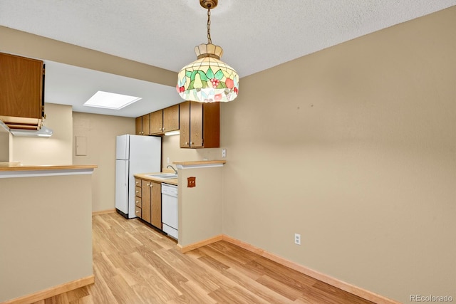 kitchen featuring light wood-type flooring, a skylight, a textured ceiling, white appliances, and sink