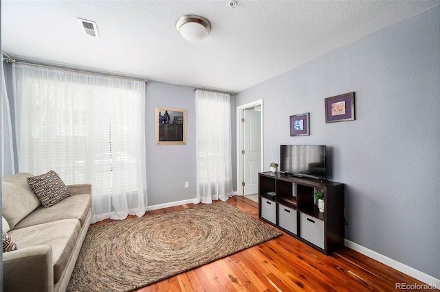 living area with baseboards, wood finished floors, and visible vents