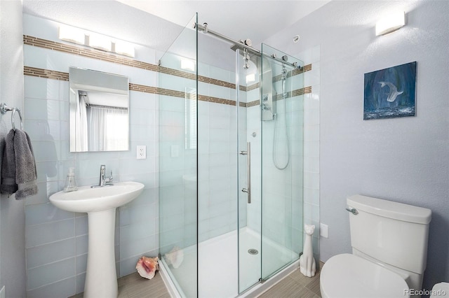 full bath with a shower stall, toilet, a sink, and tile walls