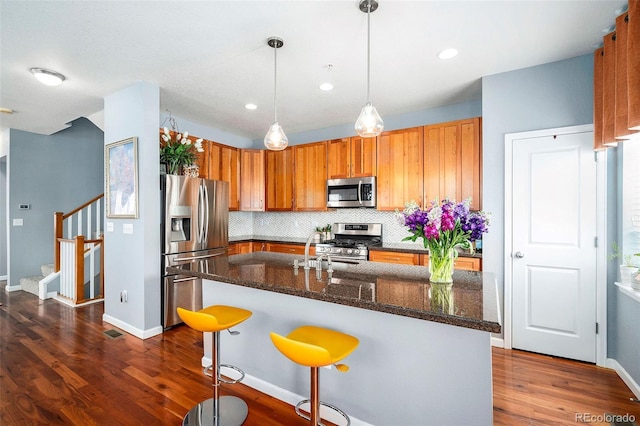kitchen with decorative backsplash, brown cabinets, pendant lighting, stainless steel appliances, and dark wood-type flooring