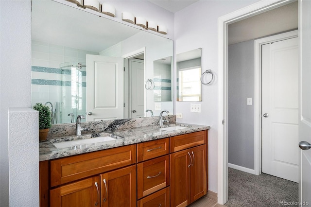 full bathroom with baseboards, a sink, double vanity, and a tile shower