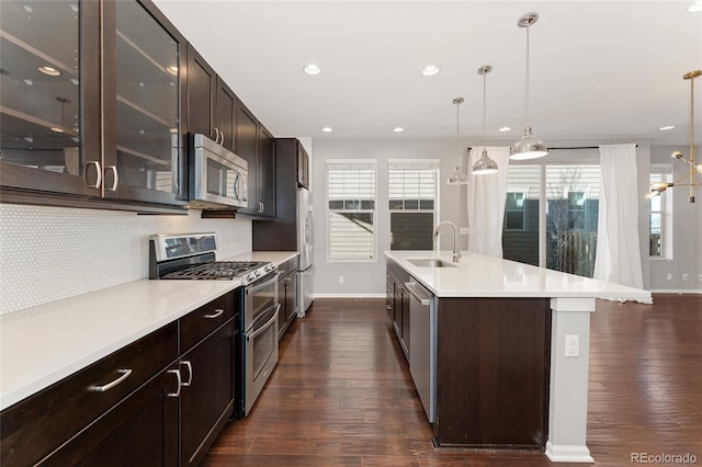 kitchen featuring appliances with stainless steel finishes, decorative backsplash, sink, hanging light fixtures, and a kitchen island with sink