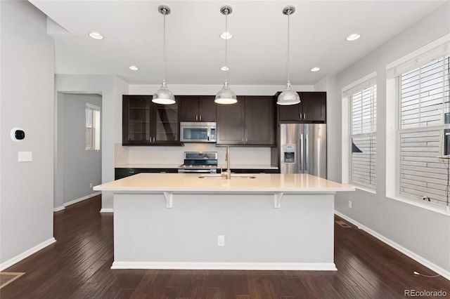 kitchen with a center island with sink, appliances with stainless steel finishes, tasteful backsplash, dark brown cabinetry, and sink