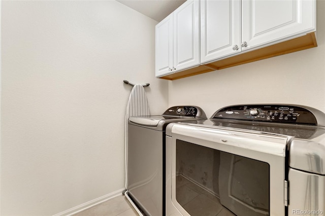 clothes washing area featuring cabinets, light tile patterned flooring, and washer and clothes dryer